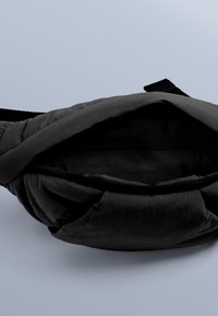 Svart midjeväska i nylon med mjuk, vadderad yta, dragkedja och justerbar rem. Insidan har en liten zip-ficka.