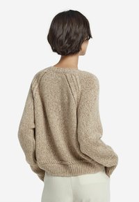 Beżowy sweter dziany o luźnym kroju, z zaokrąglonym dekoltem i ściągaczem na dole. Wyjątkowy wzór teksturowy oraz obniżone szwy na ramionach.