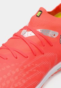 Klar rød atletiksko med tekstureret overdel, glatte detaljer og kontrasterende sølvacceter. Har tynde snørebånd og et lavt profil design.