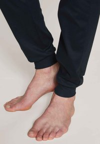 Marineblauwe joggingsbroek met gestructureerde boorden, zichtbaar bij de enkels, waardoor blote voeten te zien zijn. Gladde textuur en elastische tailleband voor comfort.
