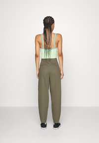 Top corto in rete verde con spalline blu abbinato a pantaloni larghi verde oliva e scarpe da ginnastica nere, visto da dietro.