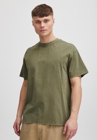 Olivengrønn T-skjorte med crew-neck laget av bomull, med korte ermer, avslappet passform og synlige sømdetaljer.