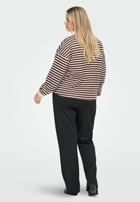 Svītrains pulovers tumši brūnā un krēmkrāsā ar garām piedurknēm, nokareniem pleciem un brīvu piegriezumu, apvienots ar vaļīgām melnām biksēm.