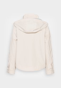Chamarra beige claro con capucha, presenta una textura suave, un diseño sencillo y costuras contrastantes; la vista trasera muestra un dobladillo redondeado.