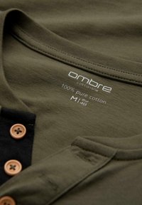 Olivegrünes Baumwoll-Henley-Shirt mit schwarzer Knopfleiste und sandfarbenen Knöpfen, Größe M, gekennzeichnet mit 100% reiner Baumwolle von der Marke Ombre.