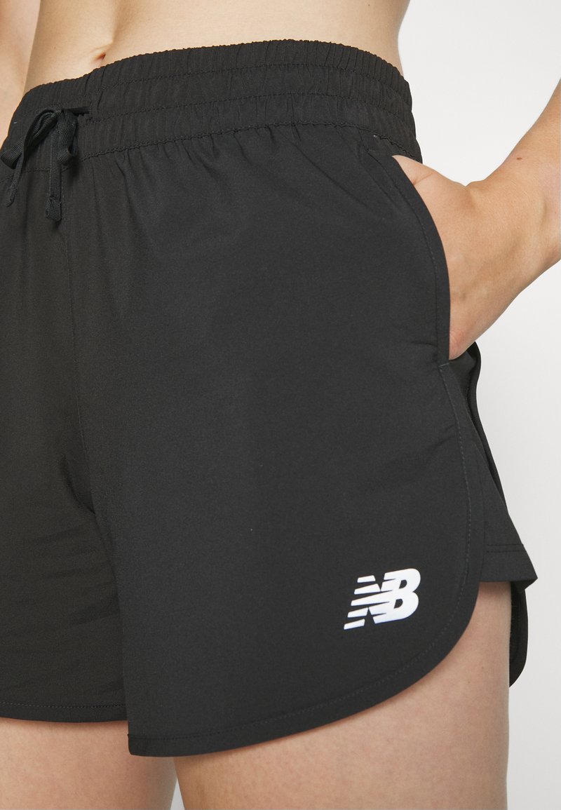 Zwarte sportshorts gemaakt van lichtgewicht materiaal met een elastische tailleband, zijzakken en een wit logo aan de onderkant aan de linkerzijde.