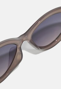 Solglasögon med en genomskinlig brun ram, överdimensionerad oval form och gradient lila linser. Slät yta utan synlig hårdvara.