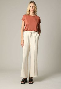 Roestkleurig T-shirt met korte mouwen, gecombineerd met tekstuurlijke ivoorkleurige wijde broekspijpen en zwarte platform sandalen; heeft een elastische taille met trekkoord.