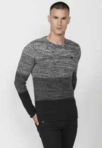 Pulover tricotat alb-negru cu un model texturat, gât rotund și mâneci lungi. Detaliu mic cu logo aproape de tiv.