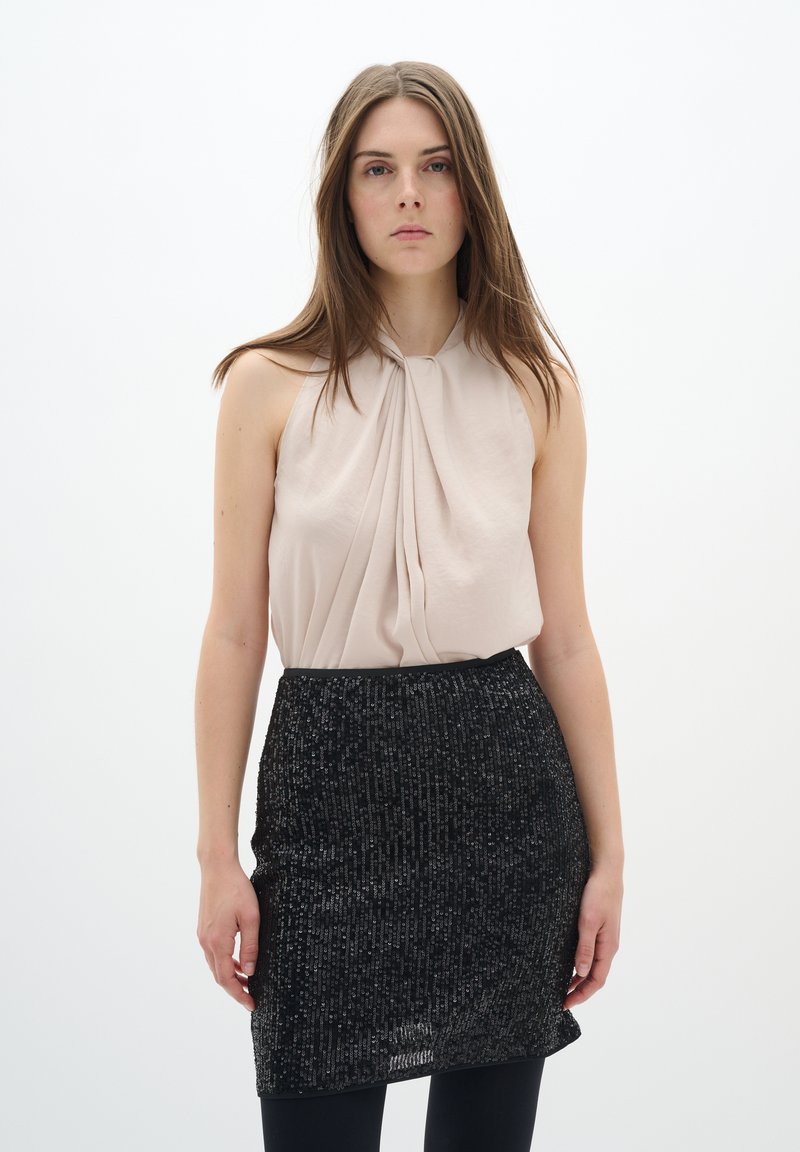 Haut halter nu avec des plis, associé à une jupe noire ajustée en sequins. Texture de tissu lisse avec un motif scintillant et une taille élastique.