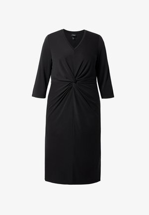 Musta mekko joustavasta kankaasta, jossa on V-pääntie, kolmanneksen mittaiset hihat ja kierretty solmu yksityiskohta vyötäröllä.