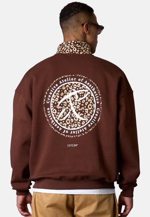 Sweatshirt marron avec col en imprimé léopard, grand graphisme circulaire avec texte et design au dos, manches côtelées et ourlet inférieur.