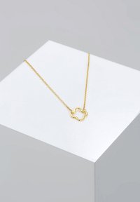 Goldene Halskette mit einem blumenförmigen Anhänger und hohlem Zentrum. Die Kette ist zart mit einer glatten Textur und vor einem neutralen Hintergrund präsentiert.
