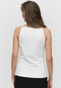Witte mouwloze top van een soepele, rekbare stof met dunne bandjes en een getailleerd ontwerp, gezien van achteren tegen een effen achtergrond.