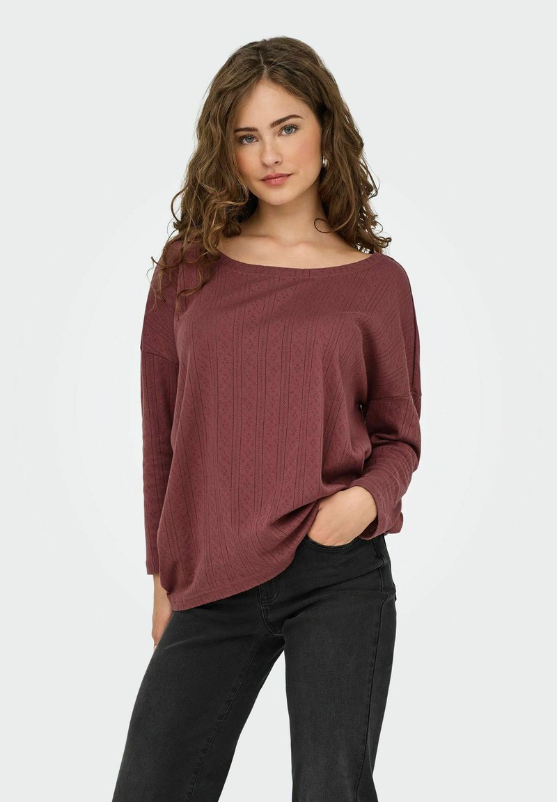 Maglione borgogna con texture, scollatura a barca, spalle scese e maniche lunghe, abbinato a jeans neri.