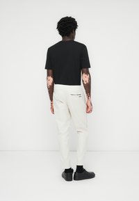 Black short-sleeve t-shirt, white tapered pants with an elastic waistband, and black shoes. Notable back pocket with a black logo.