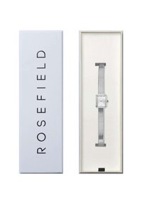 Montre en argent à cadran carré blanc et bracelet en maille argentée, présentée dans une boîte blanche avec des lettres noires.