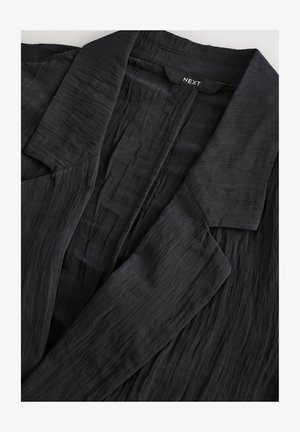 Czarna strukturalna marynarka z kołnierzem lapelowym. Wykonana z lekkiego materiału, posiada lekko pomarszczoną powierzchnię i brak widocznych zapięć.