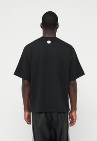 Tricou negru cu mânecă scurtă, având guler rotund și un mic logo pe spate. Fabricat dintr-un material moale, cu o croială relaxată.