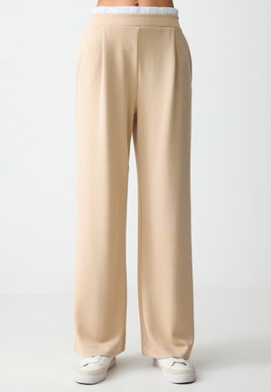 Pantaloni beige a gamba larga realizzati in tessuto morbido con un fit rilassato. Presentano una morbida cintura elastica e pieghe sottili nella parte anteriore.