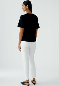 Zwarte korte mouwen top gecombineerd met witte slim-fit jeans en zwarte platte schoenen. Glad stof, ontspannen ontwerp en een perfecte pasvorm accentueren de silhouet.