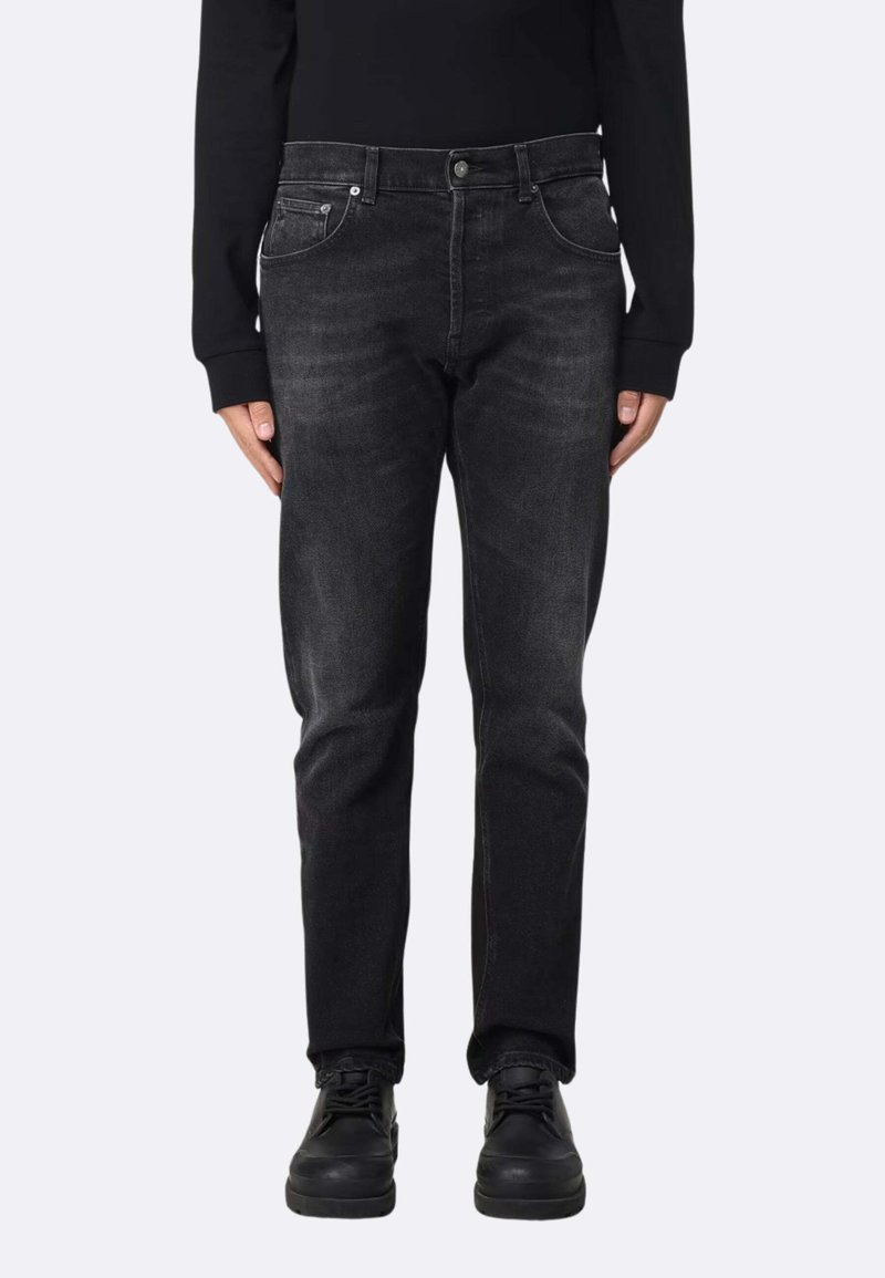 Jean en denim noir à coupe slim, avec cinq poches, coutures ton sur ton et décoloration subtile, associé à des baskets noires et une chemise à manches longues.