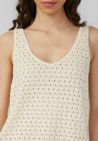 Gehaakt crèmekleurig tanktop met een V-hals en een opengewerkt patroon met diamanten vormen, dat een lichte en gestructureerde uitstraling benadrukt.