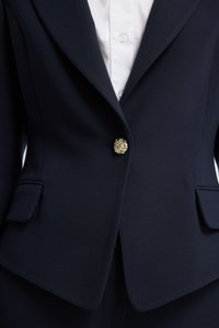 Námořnická blazerka se strukturovaným designem, zdobená výrazným zlatým knoflíkem ve tvaru lva a dvěma předními kapsami. Hladká, texturovaná tkanina.