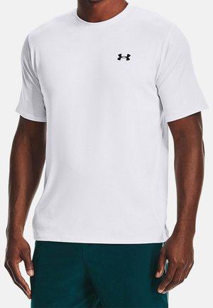 Uomo che indossa una maglietta sportiva bianca a maniche corte con un piccolo logo Under Armour nero sul petto, abbinata a pantaloncini verde scuro.