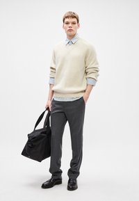 Κρεμ ριμπ πουλόβερ πάνω από ένα ανοιχτό μπλε ριγέ πουκάμισο, γκρι παντελόνι, μαύρη τσάντα και παπούτσια. Καθαρές γραμμές, ανάλαφρη εφαρμογή και ουδέτερα χρώματα.