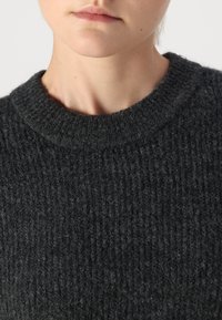 Σκούρο γκρίζο πλεκτό πουλόβερ με υφαντή υφή και στρογγυλή λαιμόκοψη. Το ύφασμα φαίνεται μαλακό και παχύ, κατάλληλο για κρύες καιρικές συνθήκες.