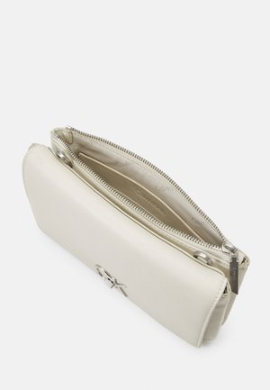 Rechthoekige clutch van crèmekleurig leer met een ritsvak en een zilverkleurig Calvin Klein-logo op de voorflap.