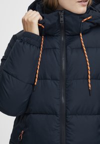 Navy puffer jacket with a high collar, featuring contrasting orange drawstrings, front zipper, and elastic cuffs for snug fit.