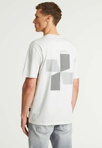 Camiseta de algodón de manga corta en gris y blanco, con un patrón geométrico de diferentes formas grises en la parte posterior.
