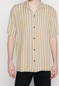 Camicia a maniche corte con bottoni in beige chiaro con righe verticali bianche. Presenta un colletto classico e bottoni neri. Vestibilità casual e trama liscia.