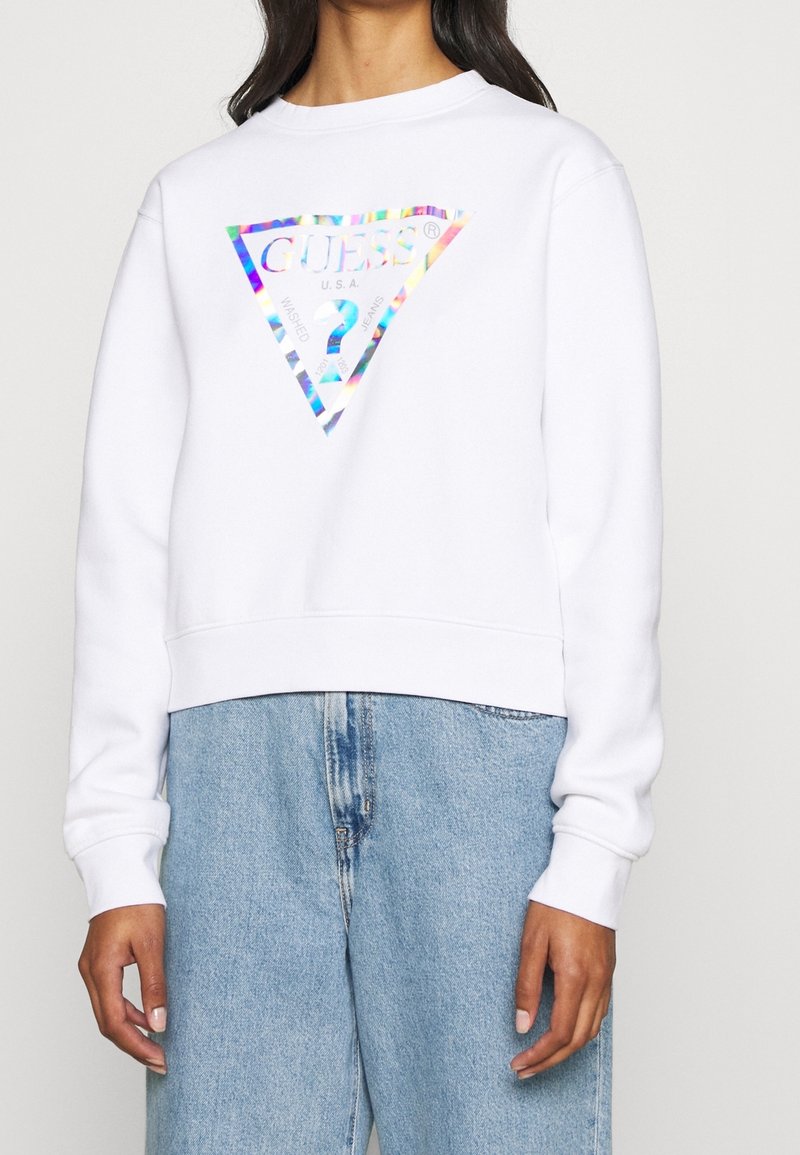 Sweatshirt court blanc avec un logo en triangle holographique, comportant le texte "GUESS U.S.A." et "WASHED". Texture douce et manches longues.