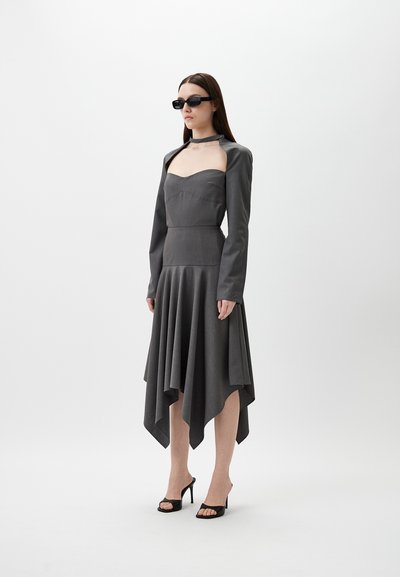 Gray asymmetrical dress with long sleeves, fitted bodice, and flowing skirt. Paired with black sunglasses and open-toe black heels.