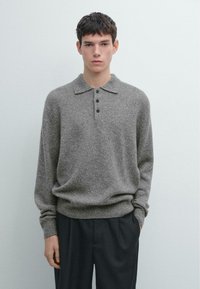 Szary dziergany sweter z kołnierzem i plisą na trzy guziki. Posiada długie rękawy i luźny krój. Całość dopełniają ciemne spodnie.