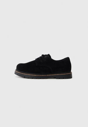 Zwarte nubuck veterschoen met een ronde neus, gladde textuur, rubberen zool en subtiele stikdetails langs de bovenrand.
