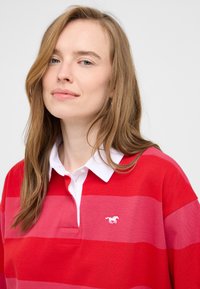 Czerwono-różowa, paskowana koszulka polo wykonana z bawełny, z białym kołnierzykiem i małym białym logo konika na piersi.