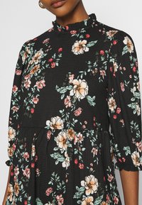 Schwarzes Blumenkleid mit Rüschenausschnitt, das große cremefarbene und rosa Blumen sowie grüne Blätter zeigt, aus strukturiertem Stoff und mit Puffärmeln.