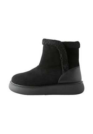 Bottines noires en daim avec un revers en fausse fourrure, dotées d'un accent en cuir lisse et d'une semelle en caoutchouc épaisse et texturée.