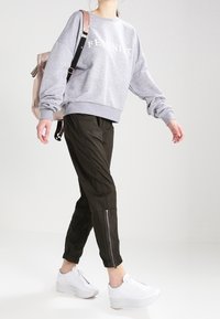 Szary sweatshirt z napisem "FEMINIST", czarne spodnie slim-fit z zamkami przy kostkach oraz białe sneakersy. Modelka niesie jasnoróżowy plecak.