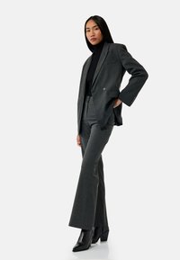 Grijze op maat gemaakte pak met een dubbelgeknoopte blazer, rechte broek en een zwarte turtleneck. Geaccentueerd met gestructureerde zwarte laarzen.