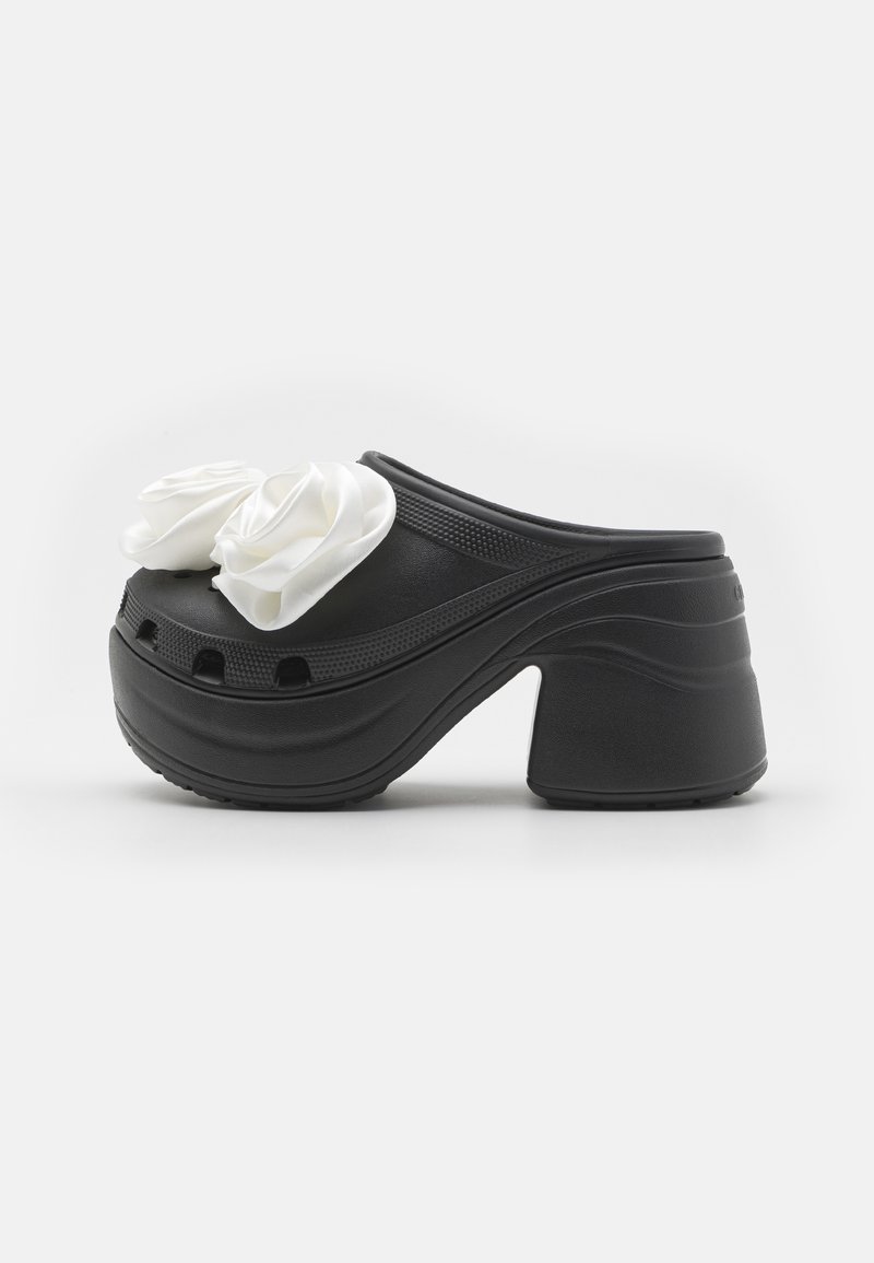 Black clogs with a chunky heel, featuring two white satin rose embellishments on the upper and ventilated holes on the front.