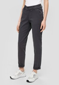 Pantalons gris foncé avec une coupe décontractée, ourlets retroussés et poches avant visibles. Portés avec des baskets blanches avec des accents gris et une tige en mesh.