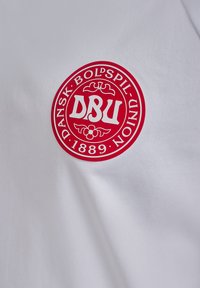 Weißes Kurzarmhemd mit einem kreisförmigen roten Logo, das "DBU" und "DANSK BOLDSPIL UNION 1889" in weißer Schrift zeigt. Glatte Textur.
