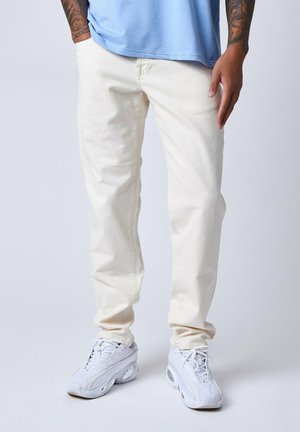 Jeans en denim blanc avec une coupe droite, dotés de cinq poches et d'une texture douce, associés à des chaussures de sport blanches et une chemise bleu clair.