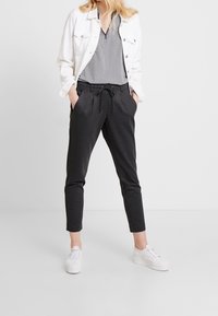 Giacca di jeans bianca, top a motivo bianco e nero, pantaloni a scacchi neri con vita elastica e tasche, abbinati a sneakers bianche.
