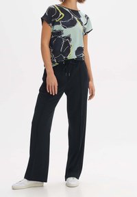 Kortärmad topp med blommönster i ljusblått med svarta och gröna detaljer, kombinerad med svarta vida byxor och vita sneakers.